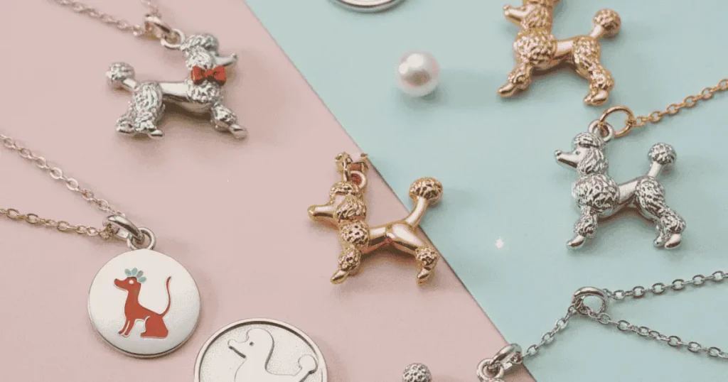 Elegant flat lay of poodle-themed jewelry charms, including gold, silver, and enamel designs, arranged on a soft pastel background with bracelets and necklaces, showcasing luxury, craftsmanship, and modern fashion style for 2025.